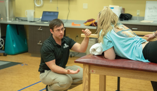 A professor engages students in hands-on learning within the PT clinic.