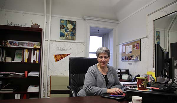 Melanie Vadzemnieks sits at her desk in her office, which features marble-tile walls as it used to be a bathroom in Old Main.