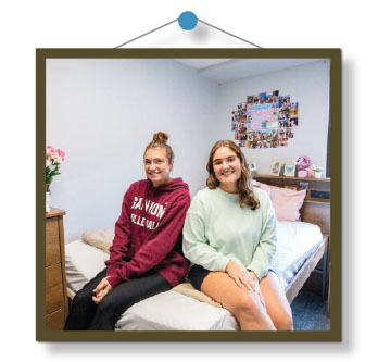 Two roommates sitting on a bed in their new dorm at South Hall